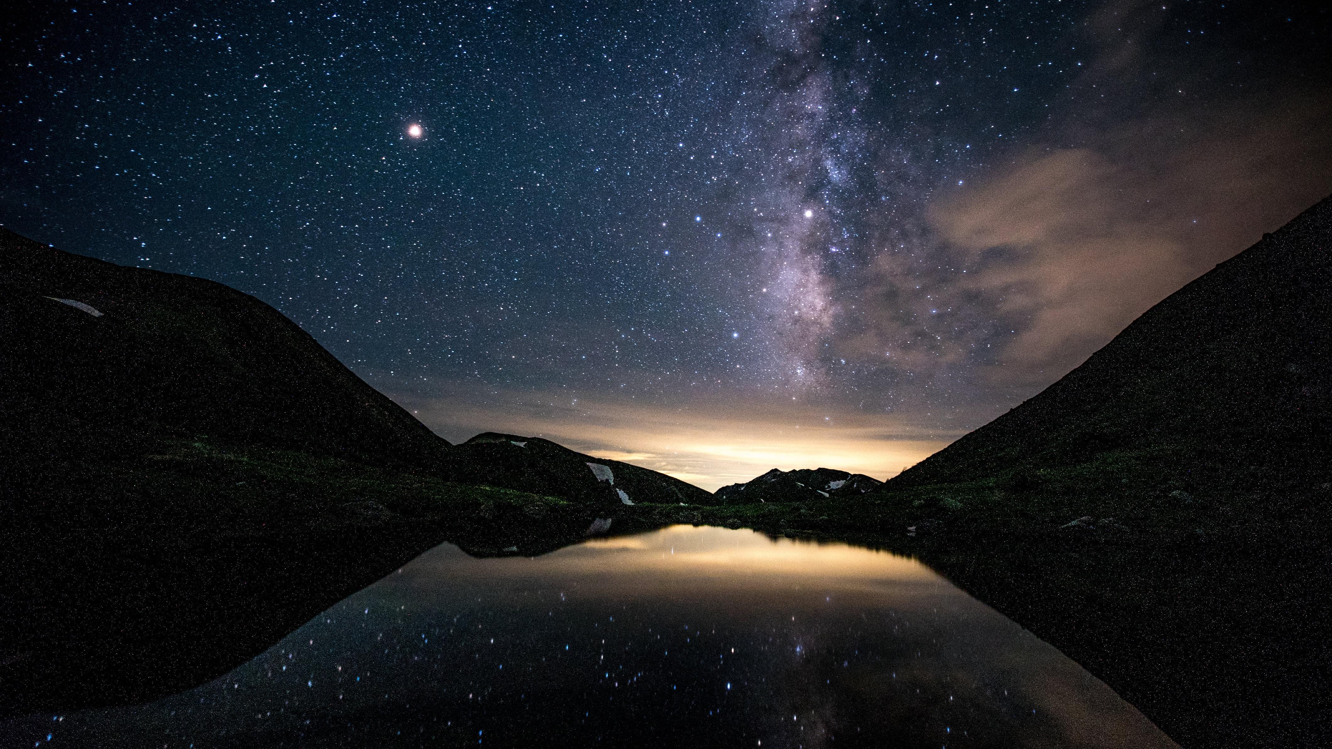 夜空に輝く無数の星と天の川が映る、美しい湖の風景。